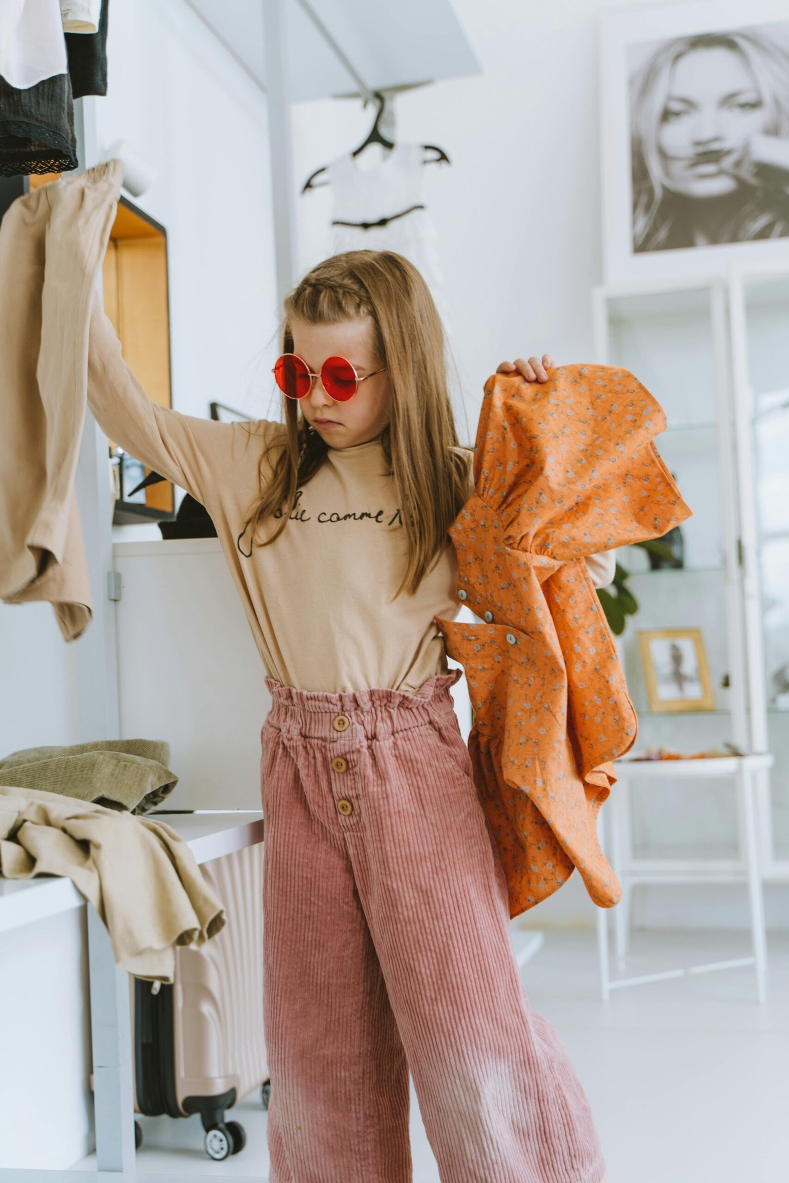 Fashionable young girl wearing stylish outfit and sunglasses in modern boutique, showcasing clothing selection.